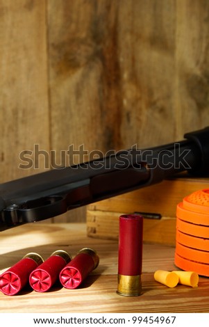 Black 12 gauge pump action shotgun with shells, clay pigeons, and ear plugs sitting next to it.