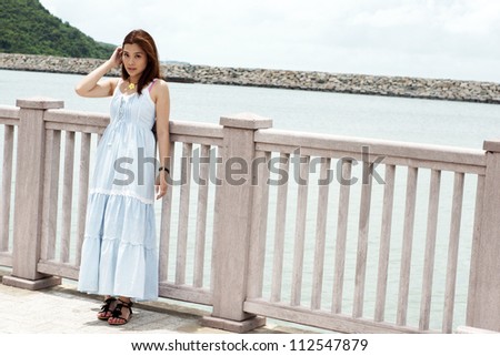 asian girl stand alone and waiting someone lying on the fences with the background of natural sea level and pier in asian oriental town