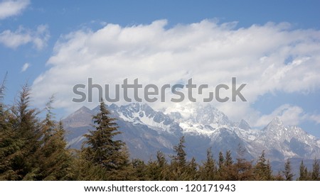 strong wind clouds in the moody sky with the snow mountain and old forests in Mount Jade Dragon or Mount Yulong