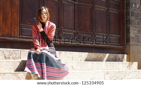 chinese girl sit on stairs and look back in sun ray in old town Lijiang in Yunnan province
