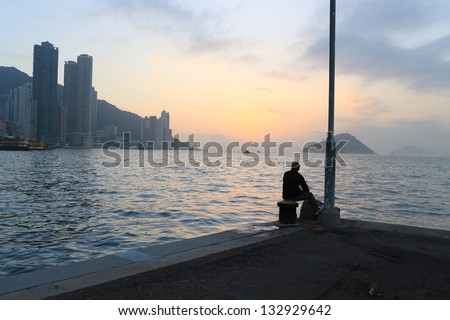 Man watching the far away sunset deep thinking in the pier waiting someone back,  with the part of Hong Kong island city, background of victoria harbour