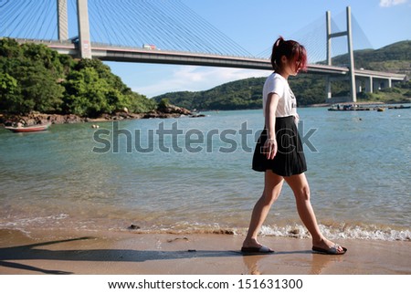 Asian girl play water on the beach, she walk with the suspension bridge background in summer, Ma Wan bay in hong kong