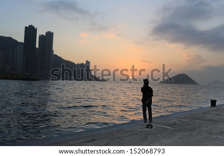 old man watching the far away under the  sunset deep thinking in the pier waiting someone back,  with the part of Hong Kong island city, beautiful background of victoria harbour