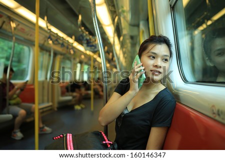 pick up the phone call go to the destination, talk on smart phone with good news, beautiful lady watch outside, in railroad box car MTR, hong kong,china, asia