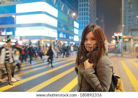Beautiful young girl stand out and watching at night in hong kong, lost in city , busy crowd and yellow zebra crossing blurred background