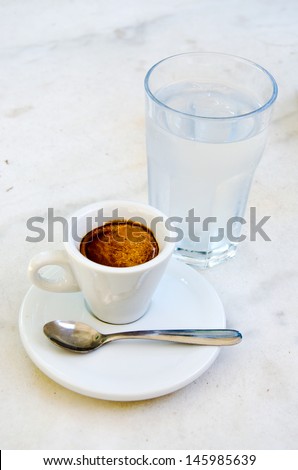 White espresso cup and glass of cold water standing on the marble table of the street cafe