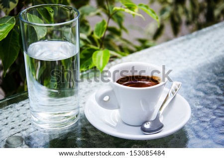 White espresso cup with glass of cold water standing on the street cafe table