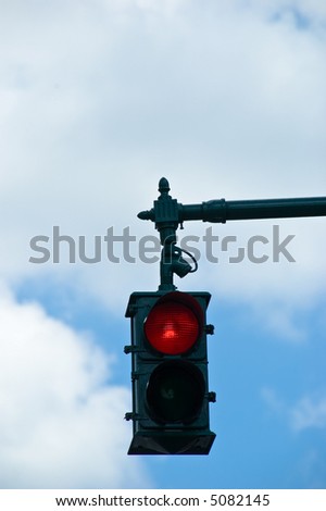 A red stop light overhead against a cloudy blue sky