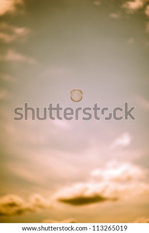 A floating bubble, just above the centre of the frame, is seen against the orange glow of an evening (or morning) sky. Vertical format with ample space for copy.