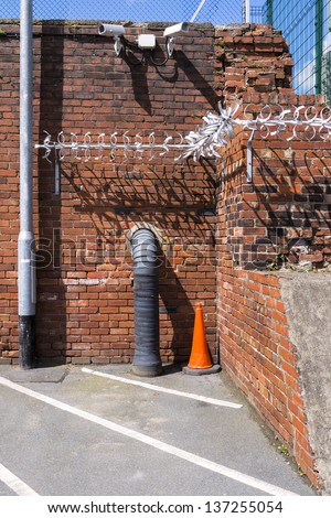 An image to illustrate security measures - closed-circuit TV cameras, chain-link fences and an anti-climb, spiked, metal contraption fixed to a brick wall.