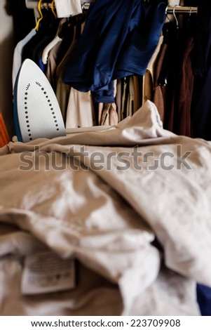 A pile of bedlinen for ironing with an electric iron amongst the linen. Vertical format.