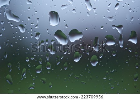 Raindrops on a window pane after heavy rain with background thrown out of focus. Horizontal format with copy space.