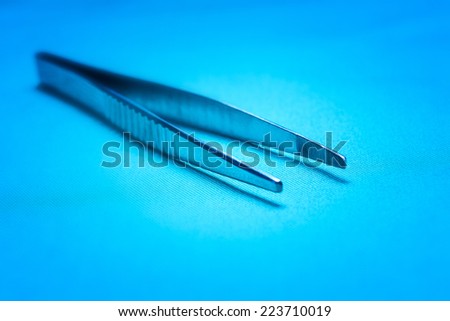 Surgical Instruments - worn, scratched surgical forceps on blue surgical drapes in clinical blue light with a shallow depth of field medical surgery. Horizontal format with copy space.