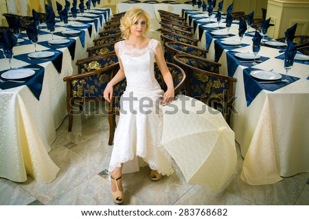 Beautiful blond bride in white dress near wedding table