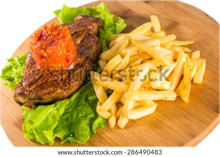 Close-up of grilled steak, french fries and lettuce on wooden board