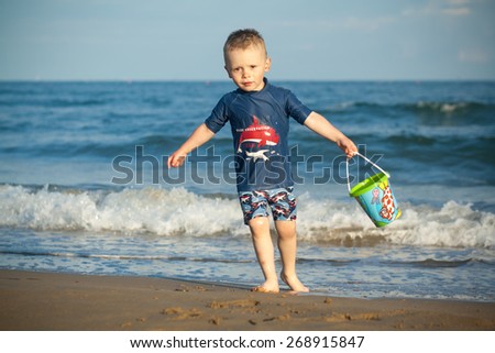 baby boy 3 years old by the sea playing with water and kid\'s pail, sea with waves background, Italy