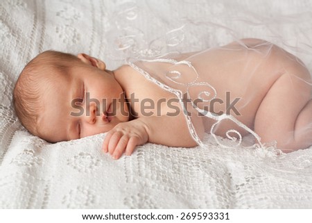 picture of a newborn baby curled up sleeping on a texture blanket, covered with translucent white textile, closed eyes