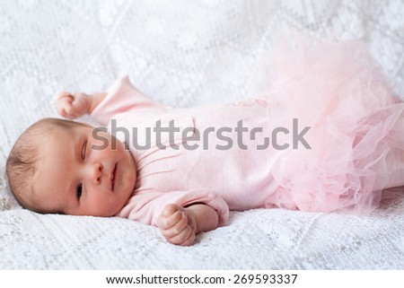 new born baby lying on texture blanket,one eye is closed, the other one is open, light pink dress with fluffy skirt