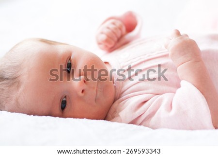 new born baby lying on texture blanket, pursed lips, light pink dress