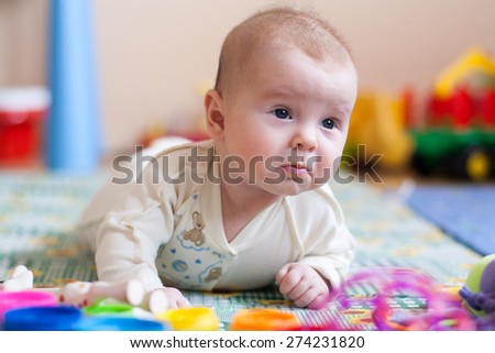 baby lying on floor with kids toys, pained expression on face, surprised expression, frustrated expression