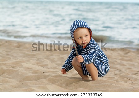 baby boy sitting on sand beach, playing with sand, dressed in marine clothes, sailor kid, sea with waves background, Bibione, Italy
