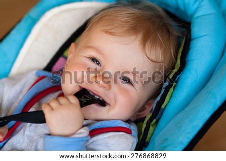 lying small baby, smiling baby, baby has something in mouth, hold with teeth, lying in deck chair for baby