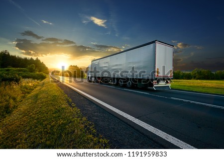 Truck driving on the asphalt road in rural landscape at sunset