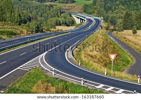 Access road to the highway between forests in the landscape, road sign right of way, in the middle of the highway electronic toll gates and bridges, view from above