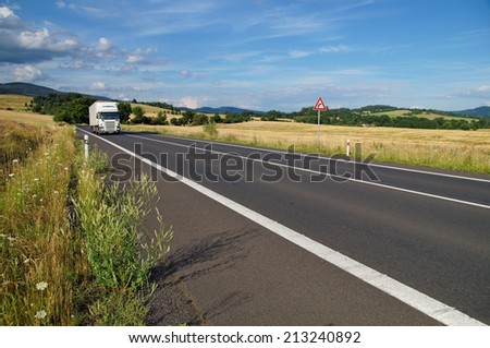 Rural landscape with road you are driving a white truck, roadside wildflowers, in the background of cornfield and wooded mountains