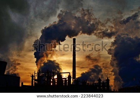 Chimneys and dark smoke over chemical factory at sunset