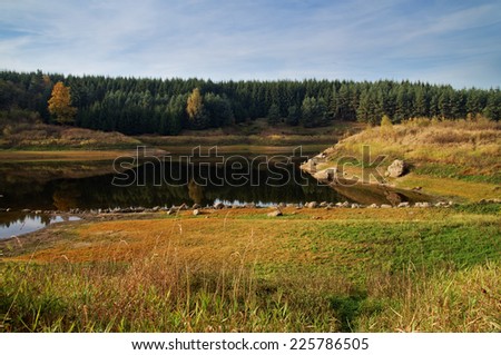 Lake in autumn landscape, on the bank of a row of stones, autumn colors