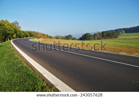 Empty asphalt road in countryside, bend of road, field in the background, forest on the horizon