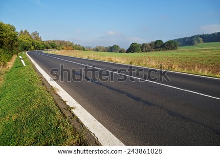 Empty asphalt road in countryside, bend of road, field in the background, forest on the horizon