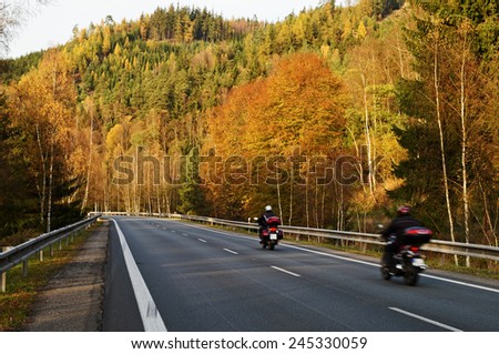 Asphalt road with a ride motorcycles in the autumn landscape, forested mountain over the road, deciduous trees with leaves in bright autumn colors