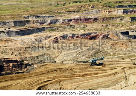 Bunk wall surface mine with exposed colored minerals and brown coal, mining equipment at the bottom the pit, view from above, top view