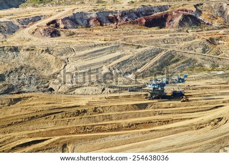 The wall surface mine with exposed colored minerals, mining equipment at the bottom the pit, view from above, top view