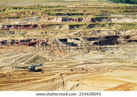 Bunk wall surface mine with exposed colored minerals and brown coal, mining equipment at the bottom the pit, view from above, top view