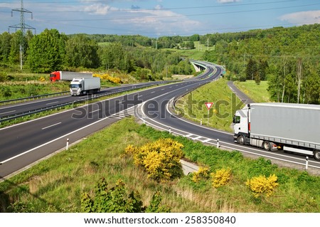 Highway in the countryside. Three moving trucks. Electronic toll gate and a bridge in the distance. View from above.
