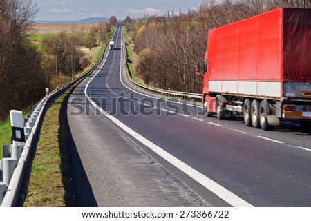 The red truck driving along an asphalt road in the countryside in early spring. White truck arrives from a distance.