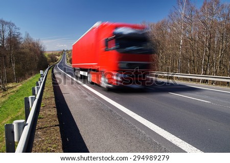 Speeding motion blur red truck on asphalt road in a rural landscape. Sunny day with blue skies.