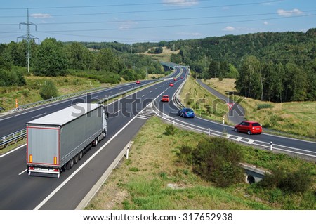 Asphalt highway with white truck and red passenger cars in wooded country. Electronic toll gate in the distance. View from above. Sunny summer day with blue skies.