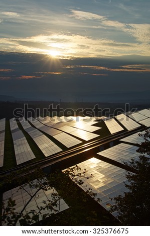Solar power plant at sunset amongst forests. The smoking smokestack and forested mountains fading into the misty haze and smog in the background.