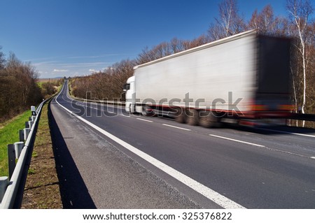 Speeding motion blur white truck on empty asphalt road in a rural landscape. Sunny day with blue skies.