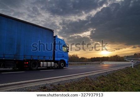 Blue truck on highway at sunset in the countryside. Dark clouds in the sky.