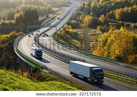 Asphalt highway with electronic toll gates in autumn woodland. Three trucks on the road. The bridge spanning the valley. View from above. Sunny day with bright fall colors.