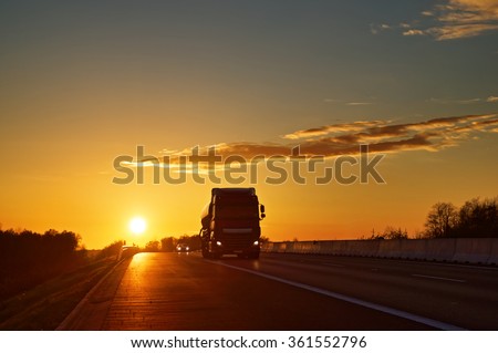 Asphalt road with oncoming truck in a rural landscape at sunset.