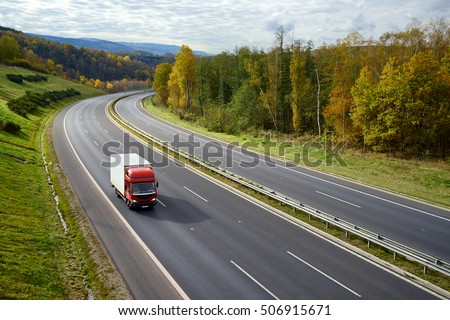 Asphalt road with a moving red small truck in the autumn landscape.