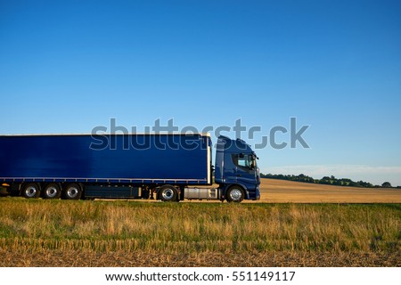 Blue truck traveling on a highway horizon along farm fields of stubble under a blue sky