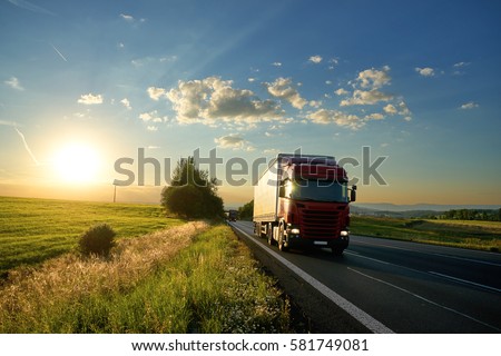 Arriving red truck on the road in a rural landscape at sunset