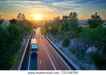 Three white trucks driving on the highway in a rural landscape at sunset. View from above.
